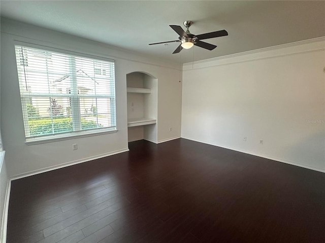 empty room with ceiling fan, dark hardwood / wood-style floors, crown molding, and built in features