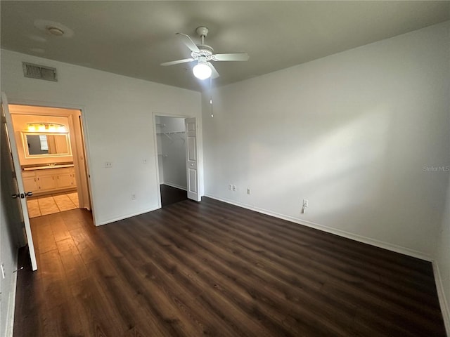 unfurnished bedroom with ceiling fan, a closet, dark wood-type flooring, and a walk in closet