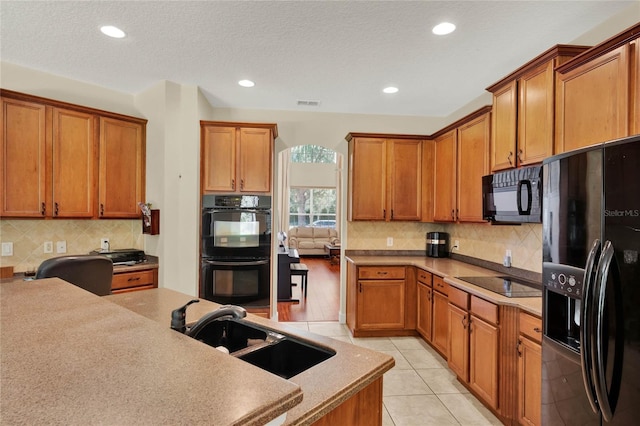 kitchen with light tile patterned floors, sink, a textured ceiling, black appliances, and decorative backsplash