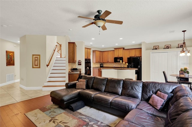 living room with a textured ceiling, ceiling fan with notable chandelier, and light hardwood / wood-style flooring