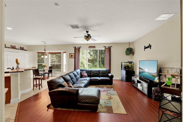 living room featuring ceiling fan, hardwood / wood-style flooring, and a textured ceiling