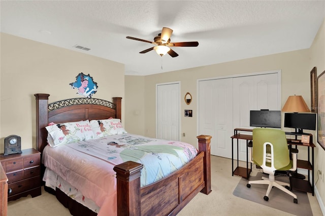 bedroom with a textured ceiling, two closets, ceiling fan, and light colored carpet