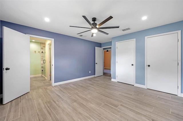 unfurnished bedroom featuring light wood-type flooring, ensuite bathroom, ceiling fan, and multiple closets