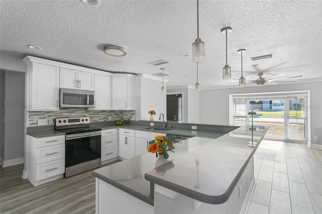 kitchen featuring sink, appliances with stainless steel finishes, pendant lighting, white cabinets, and ornamental molding