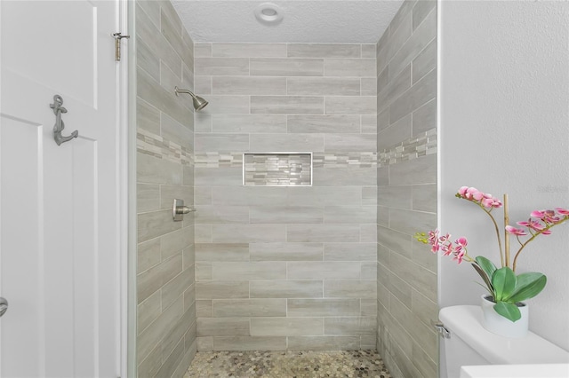 bathroom with toilet, a textured ceiling, and tiled shower