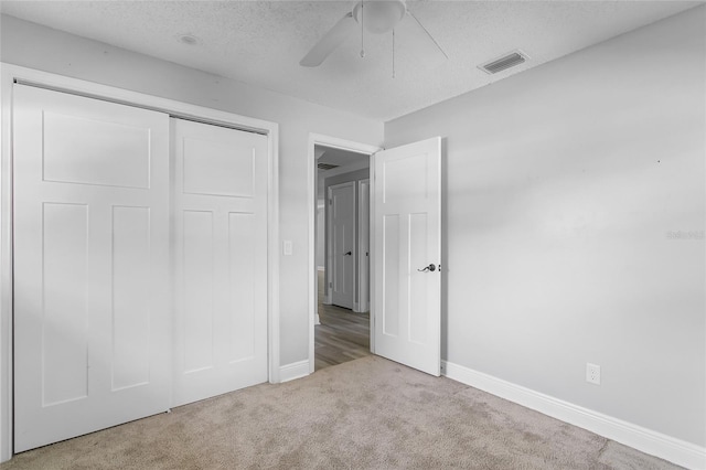 unfurnished bedroom with a textured ceiling, a closet, light colored carpet, and ceiling fan