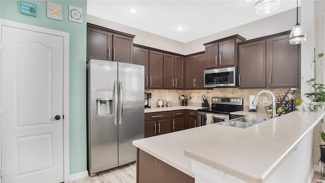 kitchen featuring kitchen peninsula, decorative backsplash, hanging light fixtures, appliances with stainless steel finishes, and sink