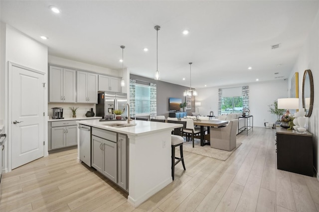 kitchen with a kitchen island with sink, light wood-type flooring, sink, and gray cabinetry