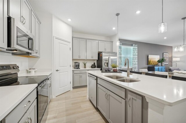 kitchen with sink, decorative light fixtures, a center island with sink, light hardwood / wood-style flooring, and appliances with stainless steel finishes