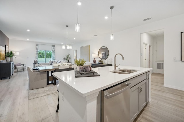 kitchen featuring an island with sink, sink, decorative light fixtures, light hardwood / wood-style flooring, and dishwasher