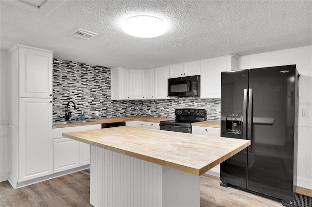 kitchen with wood counters, black appliances, sink, light hardwood / wood-style floors, and white cabinetry