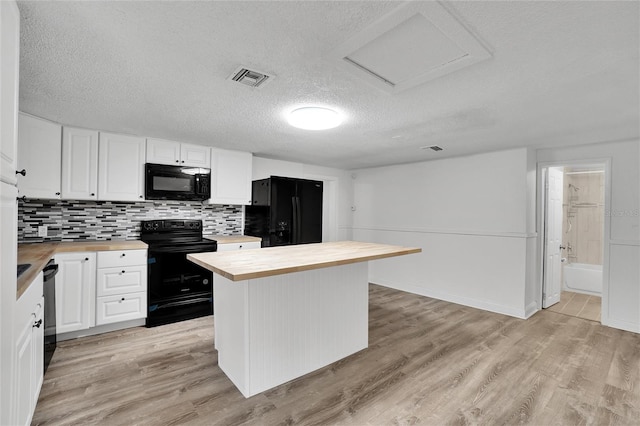 kitchen with white cabinets, butcher block countertops, light hardwood / wood-style floors, and black appliances