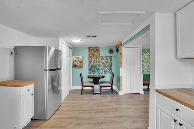 kitchen featuring butcher block countertops, stainless steel fridge, white cabinets, and light wood-type flooring