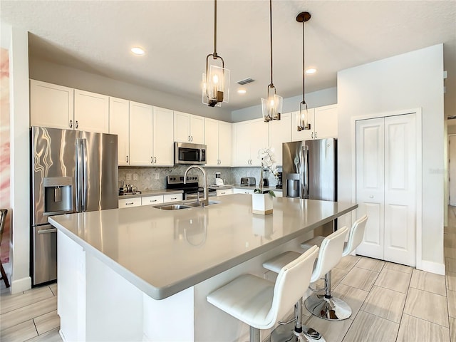 kitchen with an island with sink, sink, white cabinetry, appliances with stainless steel finishes, and decorative backsplash