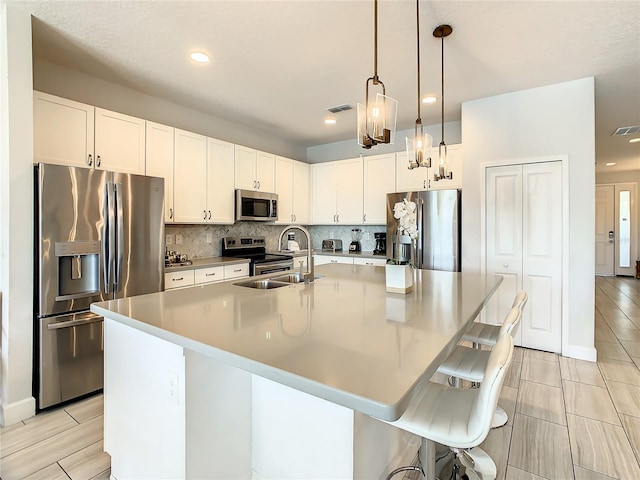 kitchen with pendant lighting, a kitchen island with sink, sink, a kitchen bar, and appliances with stainless steel finishes