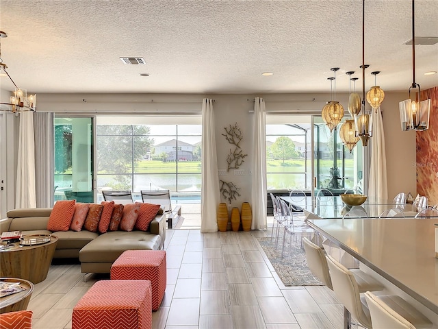 living room featuring an inviting chandelier, a water view, and a textured ceiling