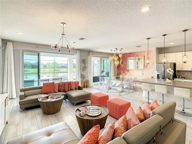 living room featuring a textured ceiling, a water view, light wood-type flooring, and an inviting chandelier