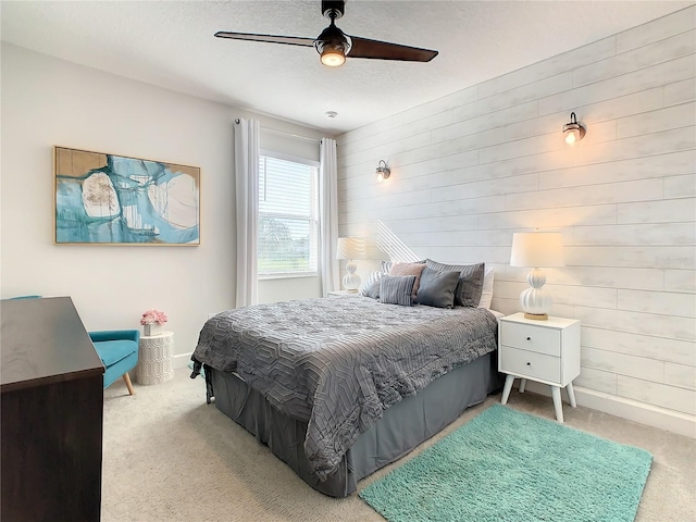 bedroom featuring ceiling fan, light colored carpet, a textured ceiling, and wood walls