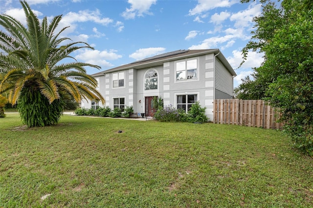 view of front of home featuring roof mounted solar panels, fence, a front lawn, and stucco siding