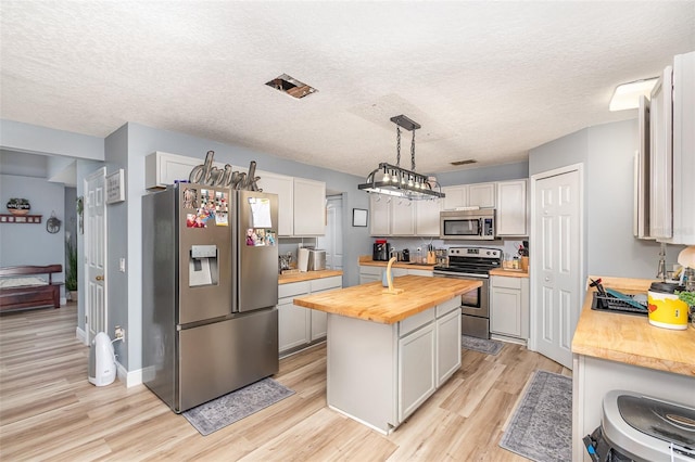 kitchen with light wood-style flooring, wood counters, appliances with stainless steel finishes, a center island, and a textured ceiling