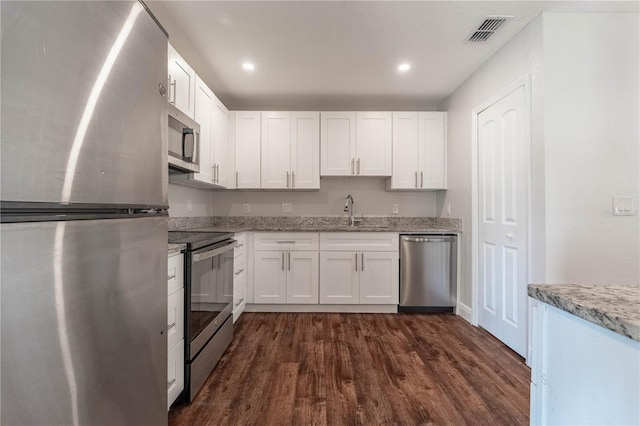 kitchen with dark wood-type flooring, sink, light stone countertops, white cabinets, and appliances with stainless steel finishes