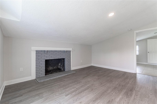 unfurnished living room featuring hardwood / wood-style floors, a textured ceiling, a fireplace, and vaulted ceiling