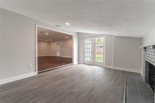 unfurnished living room featuring french doors, dark wood-type flooring, a fireplace, and a textured ceiling