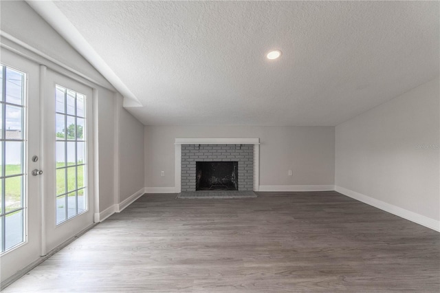 unfurnished living room featuring dark wood-type flooring, a brick fireplace, and a textured ceiling