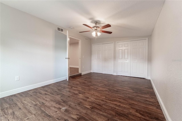 unfurnished bedroom with dark wood-type flooring, ceiling fan, multiple closets, and a textured ceiling