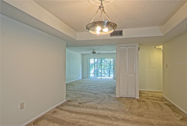 corridor with a textured ceiling, a raised ceiling, and light colored carpet