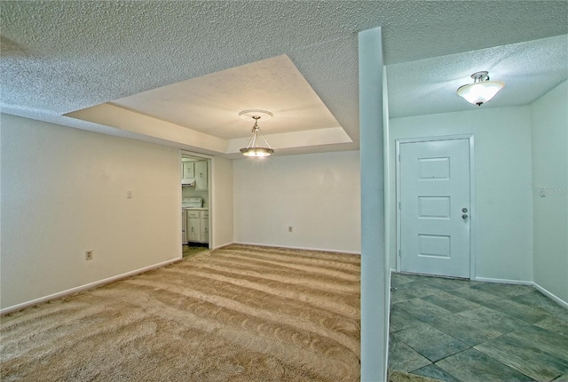 empty room with a tray ceiling, a textured ceiling, and carpet flooring