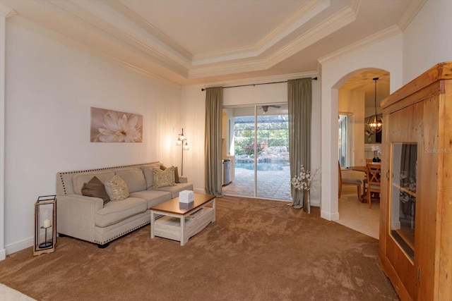 carpeted living room with an inviting chandelier, a tray ceiling, and ornamental molding