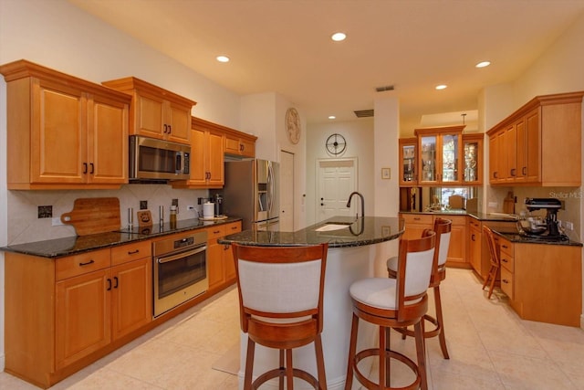 kitchen with decorative backsplash, dark stone countertops, a center island with sink, and appliances with stainless steel finishes