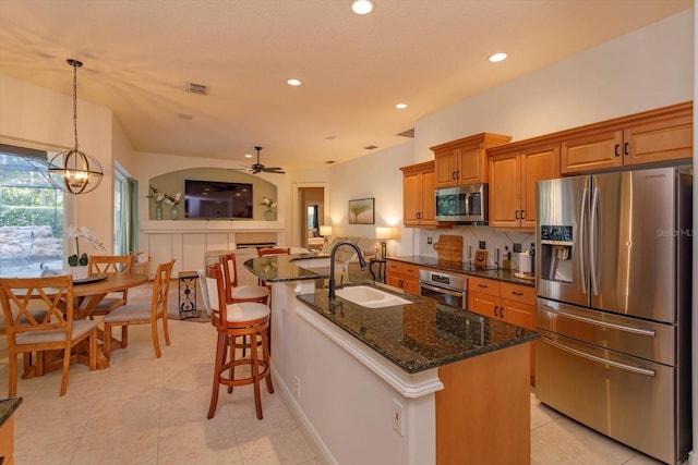 kitchen with ceiling fan with notable chandelier, pendant lighting, stainless steel appliances, a kitchen island with sink, and sink