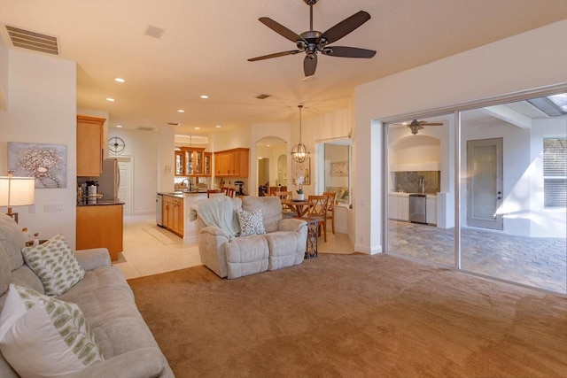 carpeted living room featuring ceiling fan with notable chandelier and sink