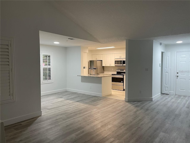 kitchen featuring appliances with stainless steel finishes, light hardwood / wood-style flooring, white cabinets, and a textured ceiling