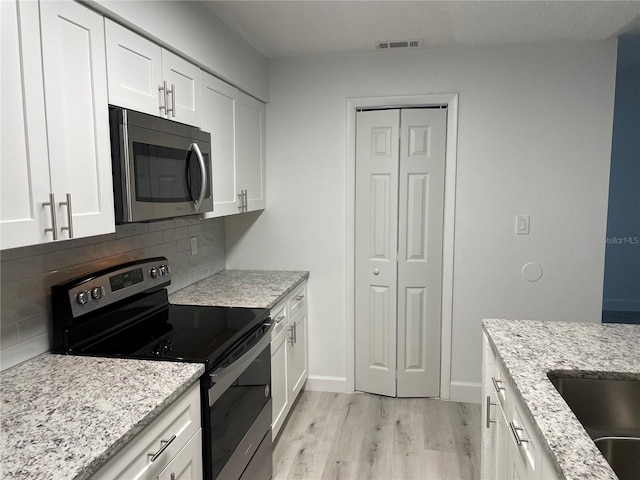 kitchen featuring white cabinets, decorative backsplash, appliances with stainless steel finishes, light hardwood / wood-style flooring, and light stone counters