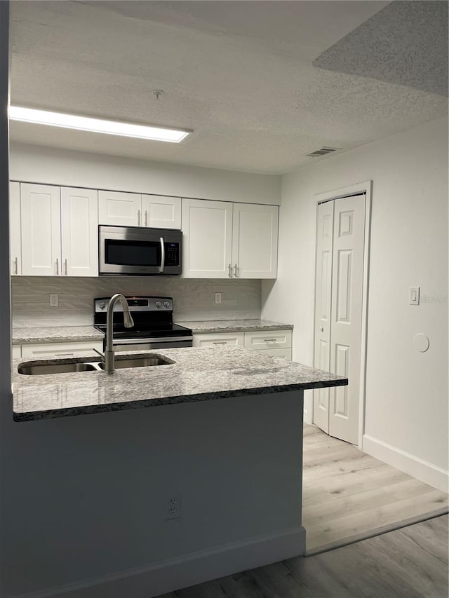 kitchen with backsplash, appliances with stainless steel finishes, white cabinetry, light wood-type flooring, and sink