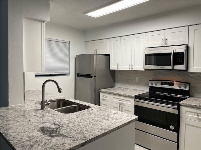 kitchen with white cabinets, tasteful backsplash, light stone countertops, sink, and stainless steel appliances