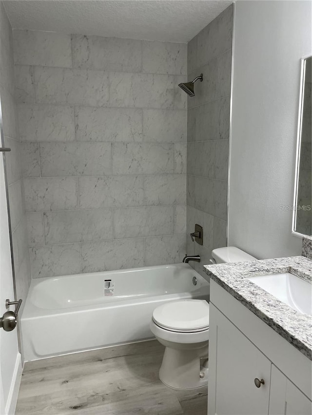 full bathroom with a textured ceiling, hardwood / wood-style flooring, toilet, vanity, and tiled shower / bath combo