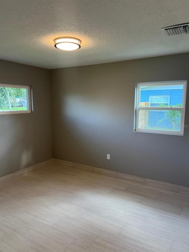 unfurnished room with a textured ceiling and light hardwood / wood-style floors