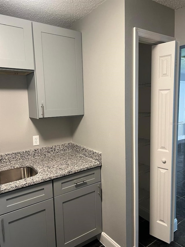 kitchen featuring gray cabinets, dark tile patterned flooring, sink, light stone counters, and a textured ceiling