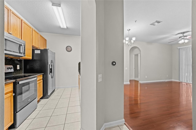 kitchen with appliances with stainless steel finishes, ceiling fan with notable chandelier, backsplash, a textured ceiling, and light hardwood / wood-style flooring