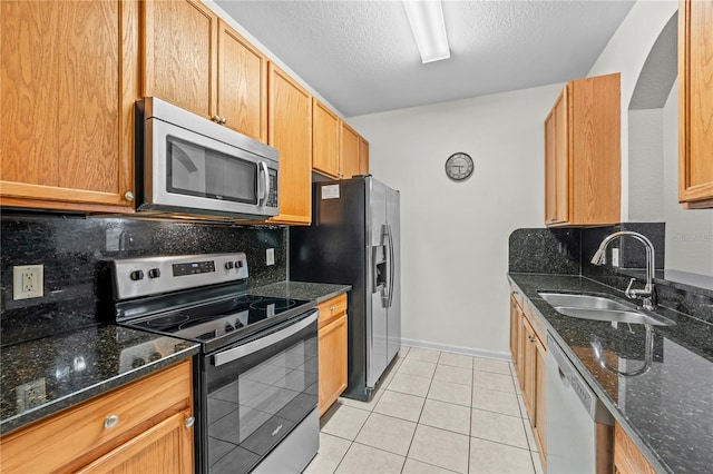 kitchen with appliances with stainless steel finishes, decorative backsplash, dark stone counters, and sink