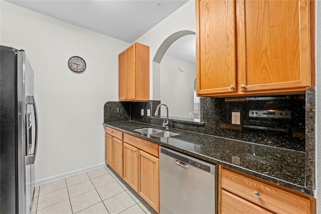 kitchen with tasteful backsplash, sink, stainless steel appliances, light tile patterned floors, and dark stone countertops