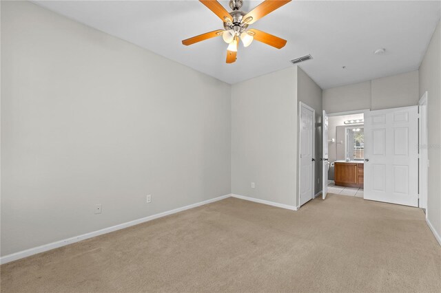 unfurnished bedroom featuring ceiling fan, ensuite bath, and light carpet