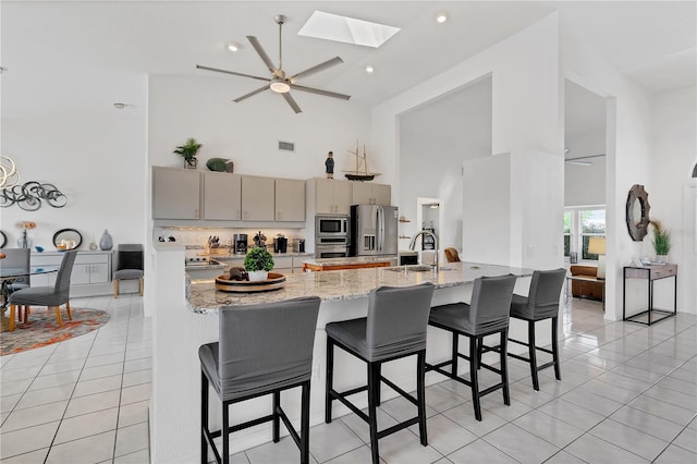 kitchen featuring light stone counters, light tile patterned floors, sink, high vaulted ceiling, and appliances with stainless steel finishes