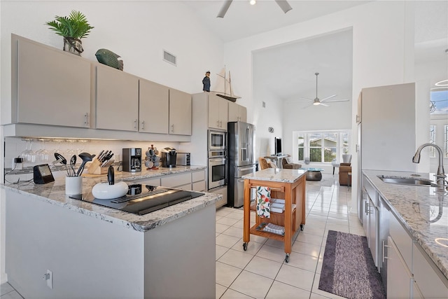 kitchen featuring sink, light stone counters, high vaulted ceiling, appliances with stainless steel finishes, and light tile patterned floors