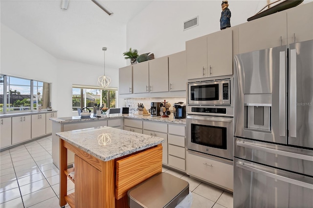 kitchen with light tile patterned floors, decorative light fixtures, high vaulted ceiling, appliances with stainless steel finishes, and a center island