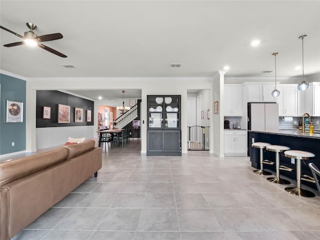 living room featuring light tile patterned floors, crown molding, sink, and ceiling fan with notable chandelier